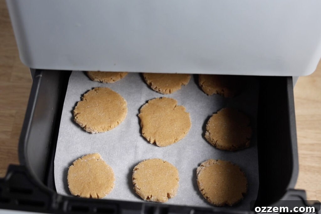 Several flattened peanut butter cookies baking evenly within the basket of an air fryer, achieving a beautiful golden-brown color.