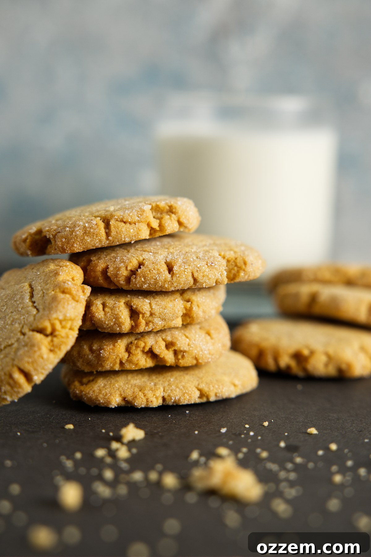 A tempting stack of golden air fryer peanut butter cookies next to a tall glass of fresh milk, with scattered cookie crumbs, creating a classic and inviting dessert scene.