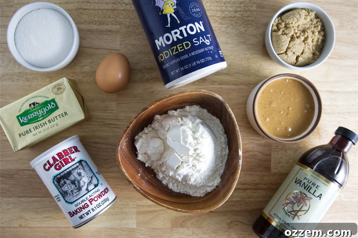 A selection of essential ingredients for making air fryer peanut butter cookies, including a jar of creamy peanut butter, sticks of butter, a bowl of flour, an egg, vanilla extract, granulated sugar, brown sugar, and baking powder, artfully arranged for a recipe demonstration.