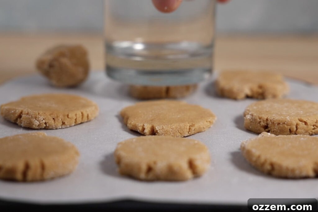 Cookie dough balls being gently pressed flat with the bottom of a glass, creating the classic textured top before air frying.
