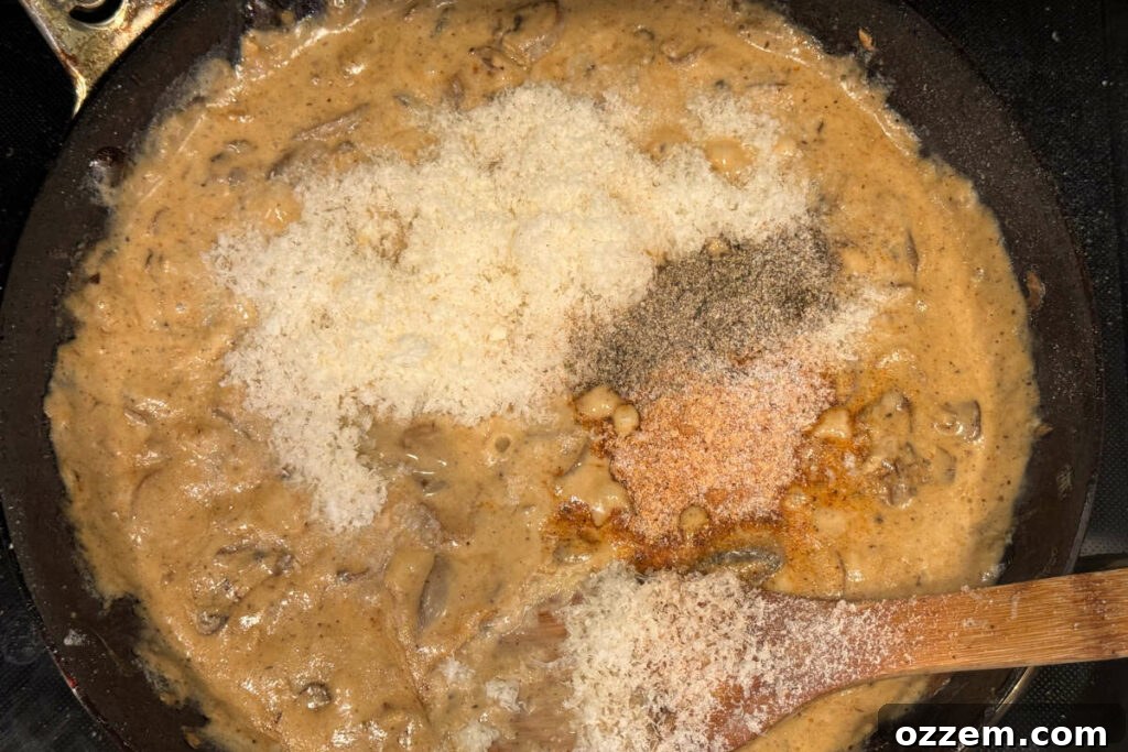 Grated Parmesan cheese and various spices being stirred into a creamy roux in a frying pan, enriching the sauce.
