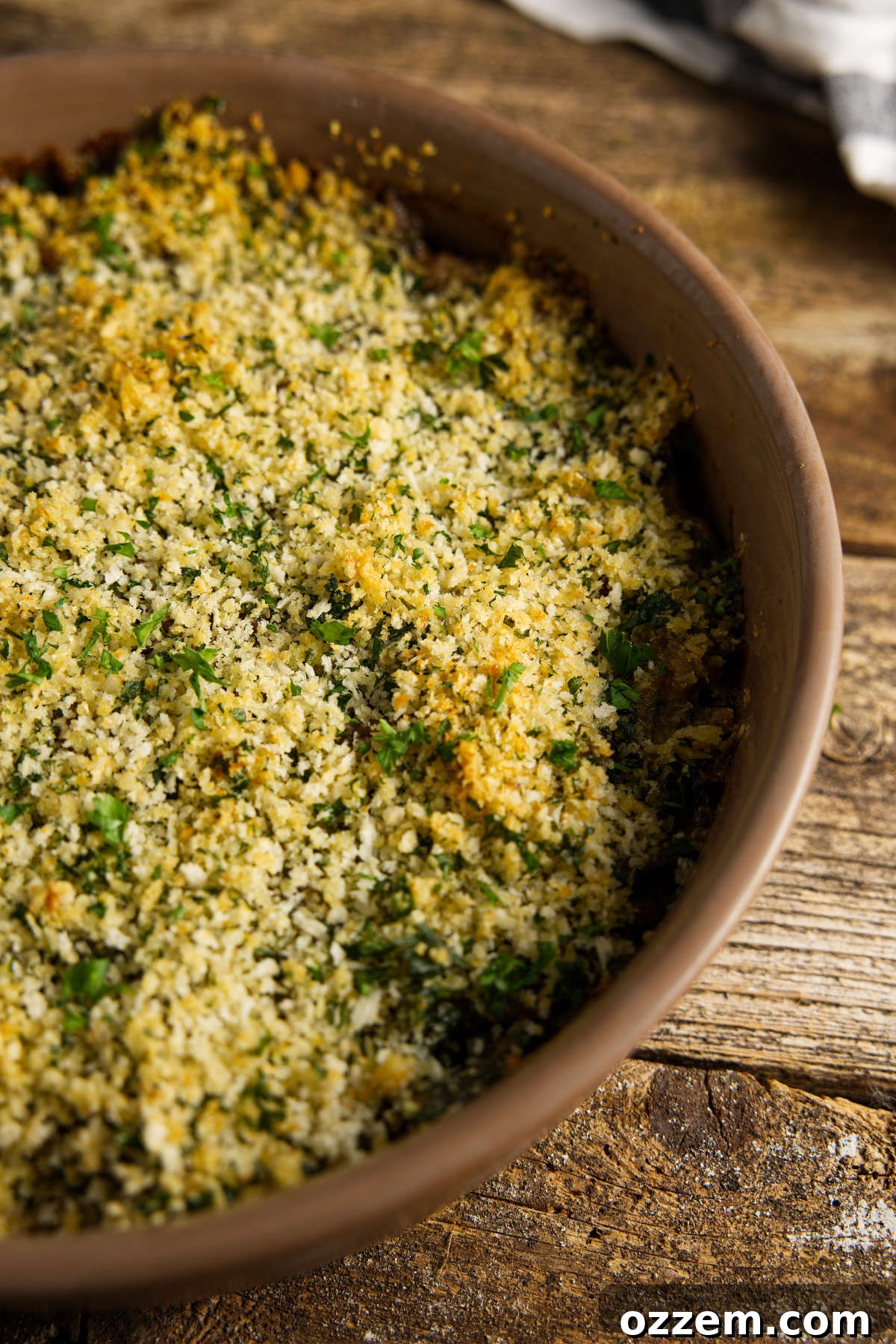 A rustic casserole dish filled with smoked green bean casserole, featuring a bubbly, creamy texture and a golden breadcrumb topping, resting on a distressed wooden plank counter.