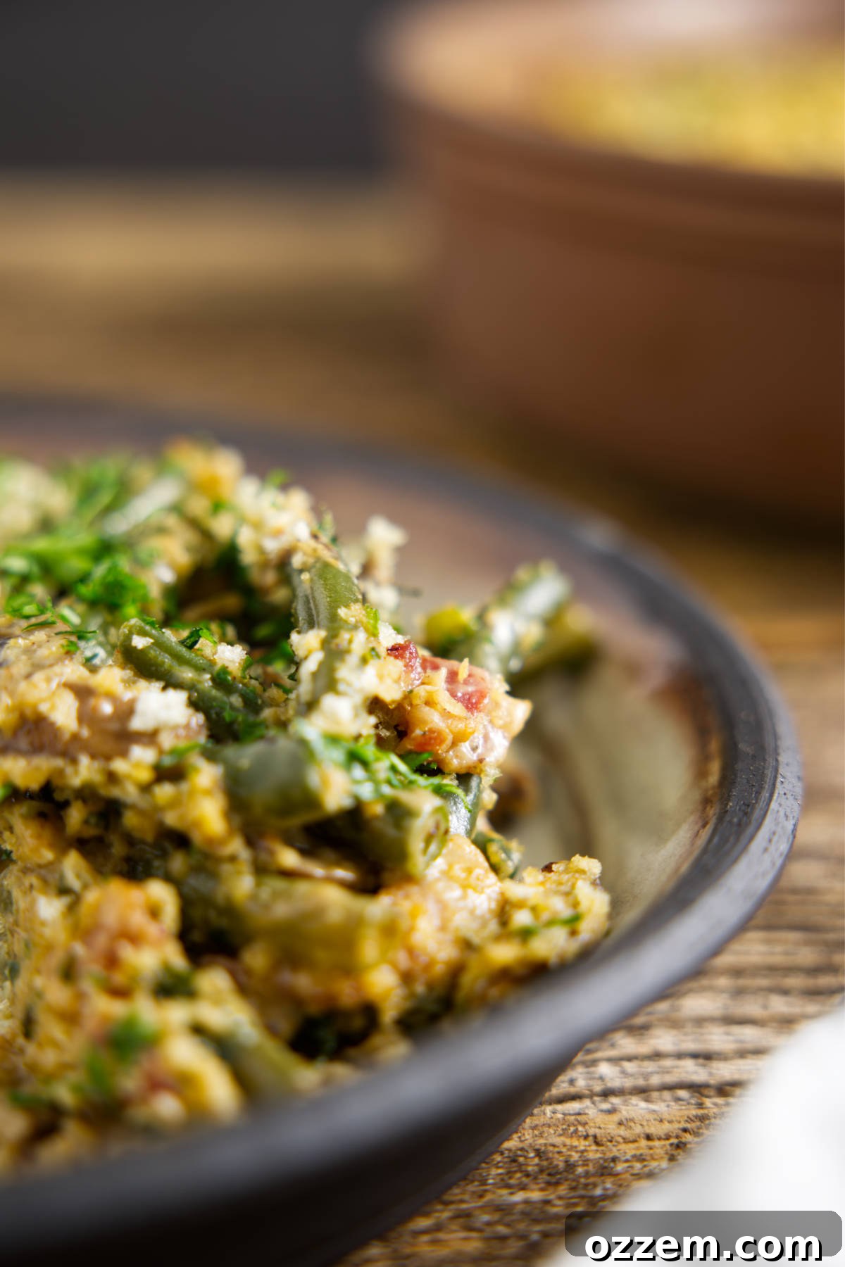 A serving of Smoked Green Bean Casserole on a white ceramic plate with a black rim, showcasing its creamy texture, green beans, and crispy topping.