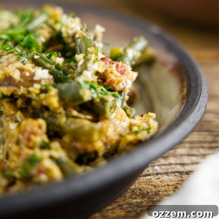Close up of Smoked Green Bean Casserole on a plate, loaded with bacon, mushrooms, and a creamy sauce with a crispy topping.