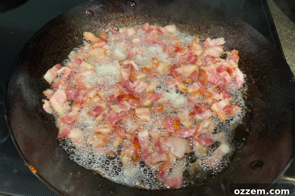 Bacon sizzling and cooking in a cast iron fry pan on a stovetop, turning golden brown and crispy.