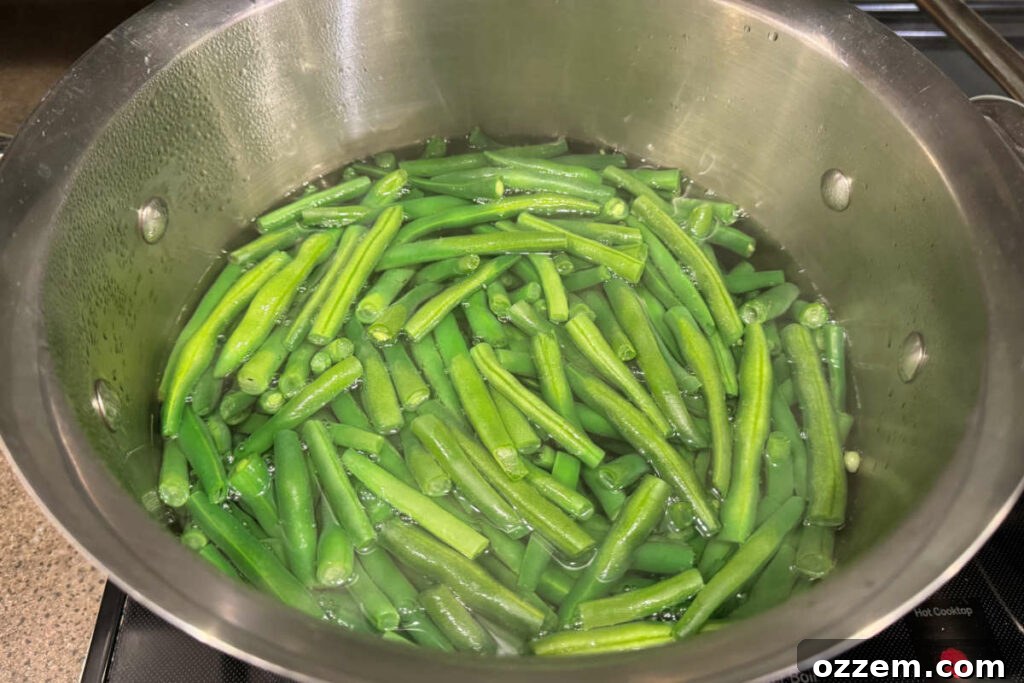 Fresh green beans boiling in a large pot of water on a stovetop, maintaining their vibrant green color.