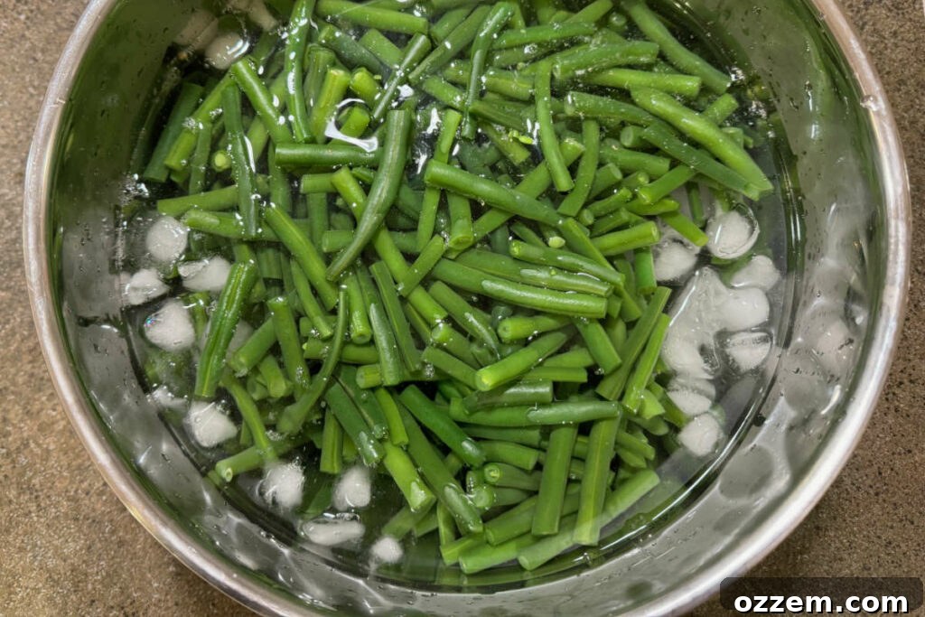 Cooked green beans being rapidly cooled in a large bowl filled with ice water to stop the cooking process.