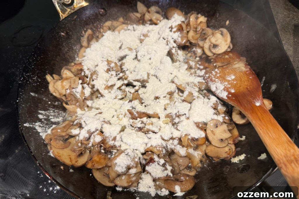 Adding all-purpose flour to cooked mushrooms and onions in a frying pan to create a roux base.
