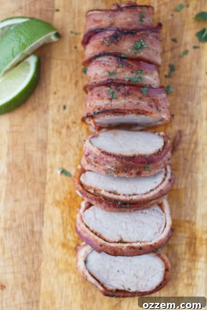 Traeger Smoked Bacon-Wrapped Pork Tenderloin 5 Bacon wrapped pork tenderloin cut into slices on wood cutting board with cilantro and lime garnish