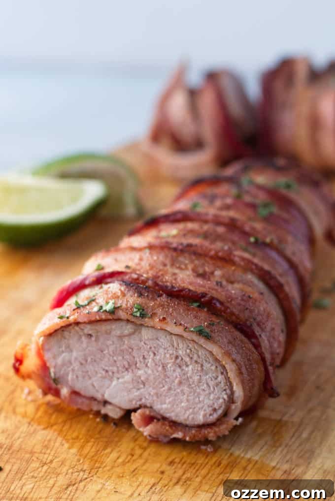 Traeger Smoked Bacon-Wrapped Pork Tenderloin 6 Bacon wrapped pork tenderloin on wood cutting board with cilantro and lime garnish