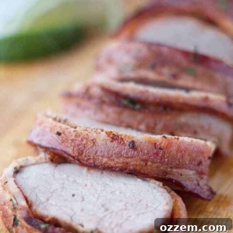 Bacon wrapped pork tenderloin cut into slices on wood cutting board with cilantro and lime garnish
