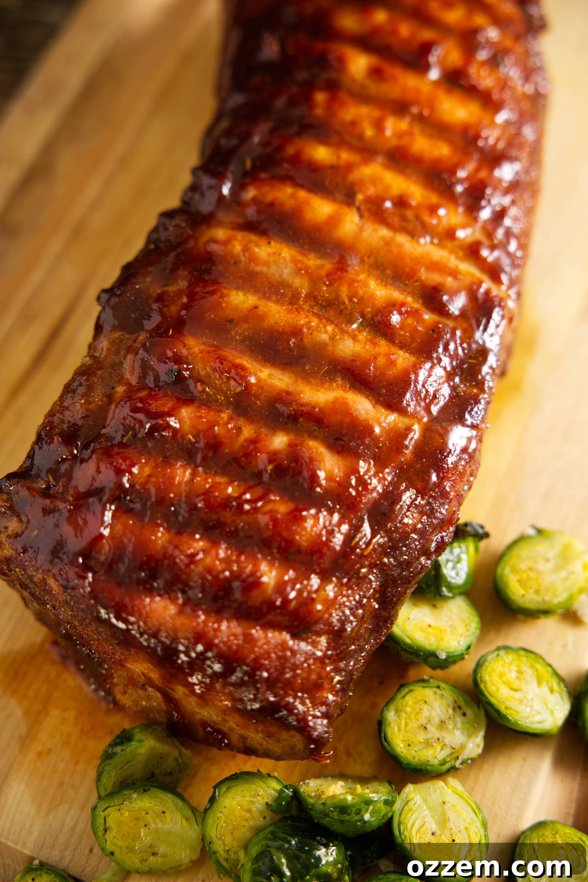Whole pork loin resting on cutting board with Brussels sprouts surrounding it.