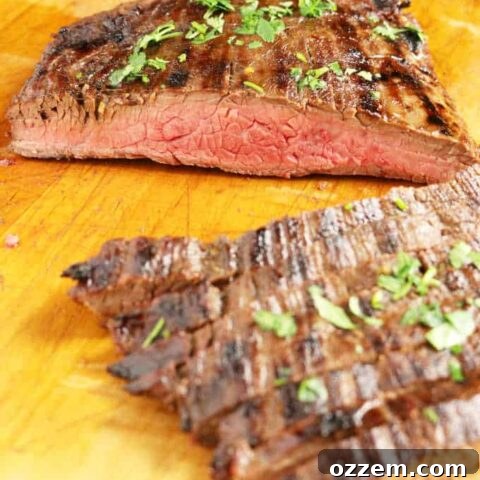 Grilled flank steak on wood cutting board sliced into strips medium rare, veggies in background