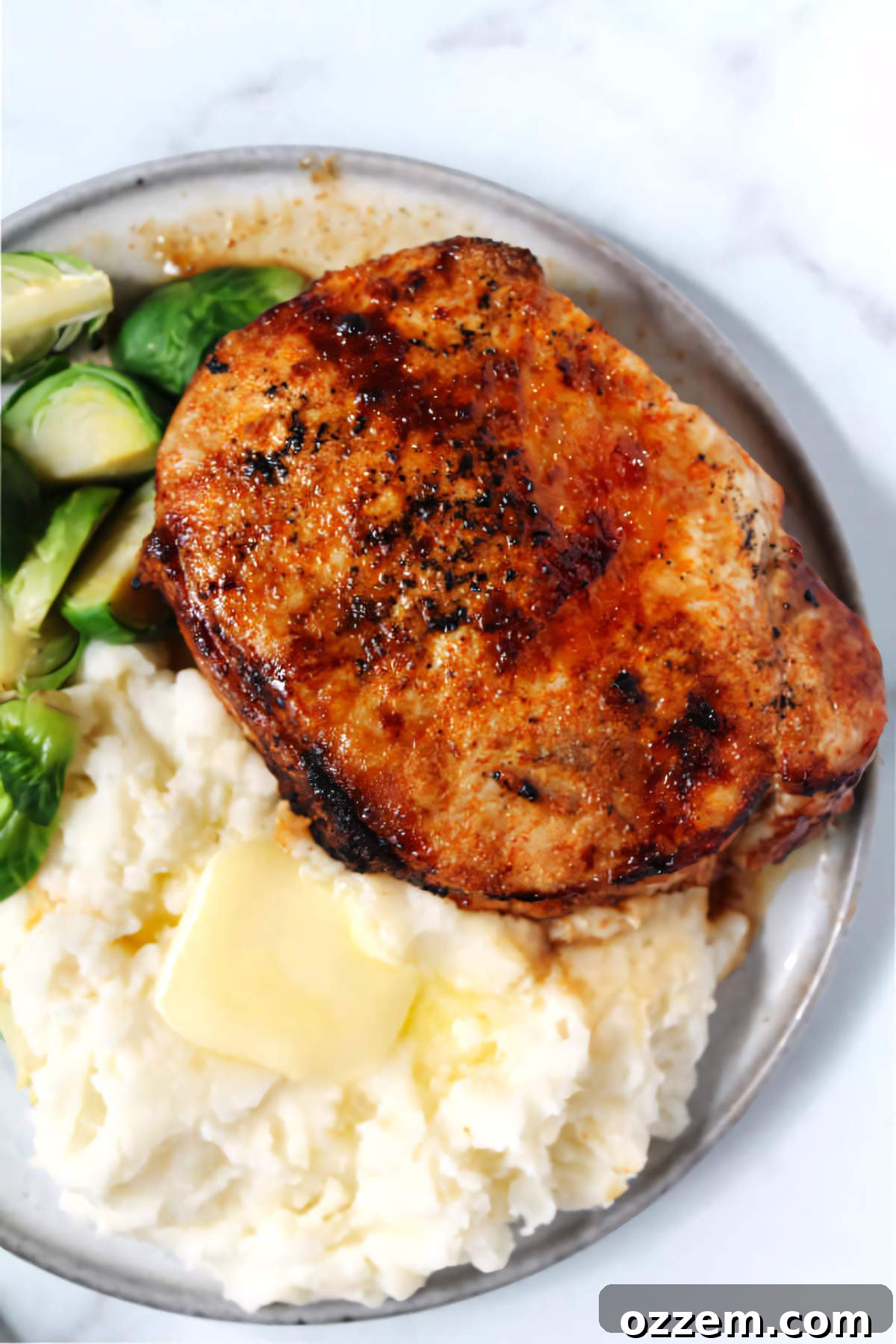 Chipotle crusted pork chop plated with mashed potatoes and Brussels sprouts.
