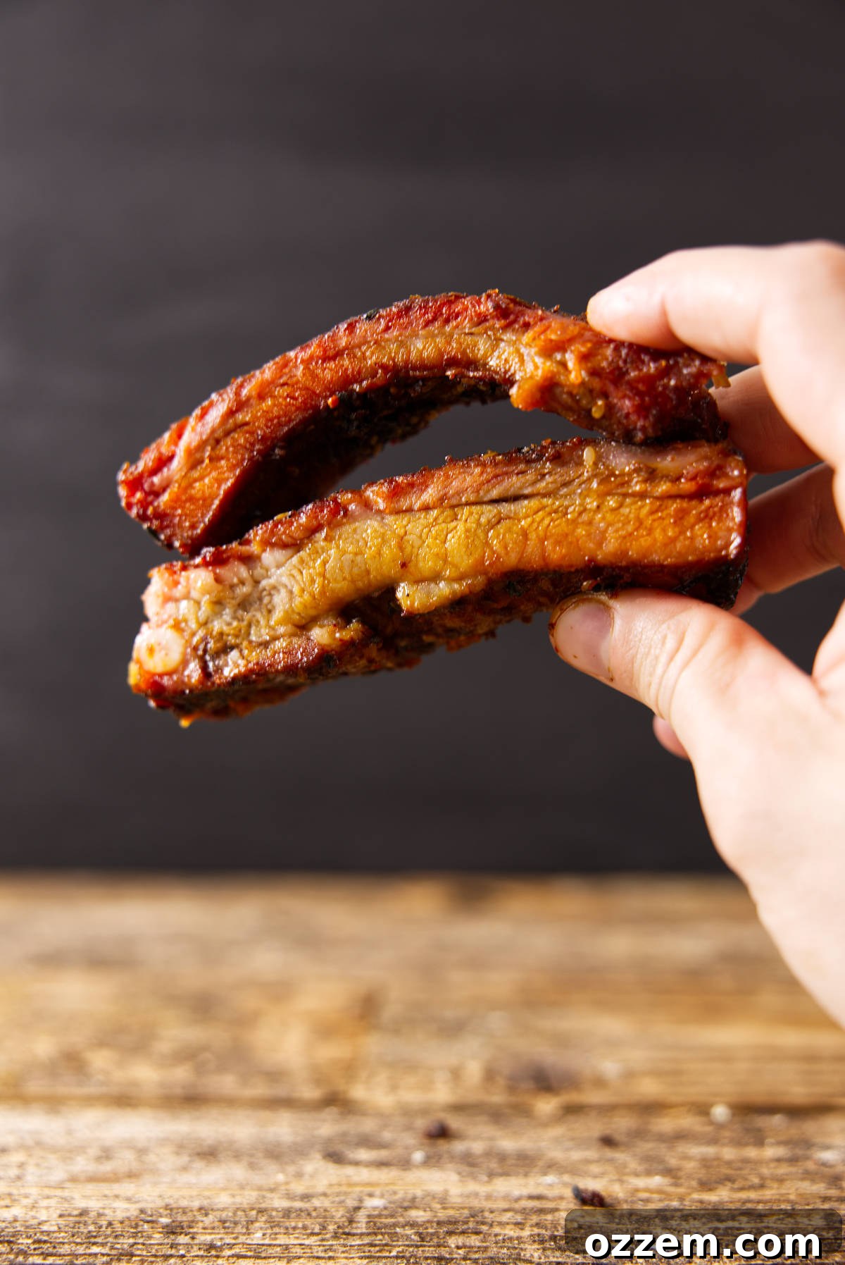 Hand holding cooked pork loin back ribs vs spare ribs.