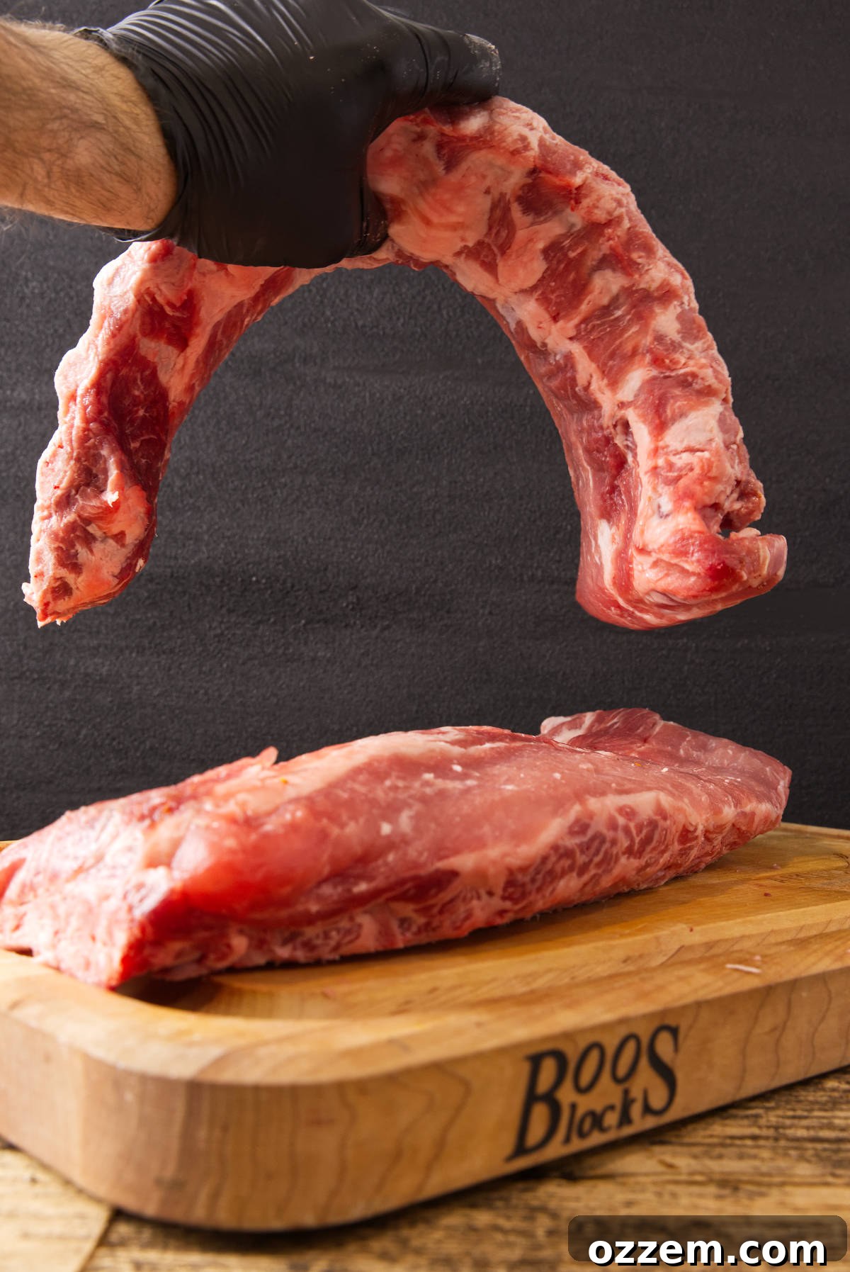 Holding pork loin back ribs have another slab of baby back ribs on a butcher block.
