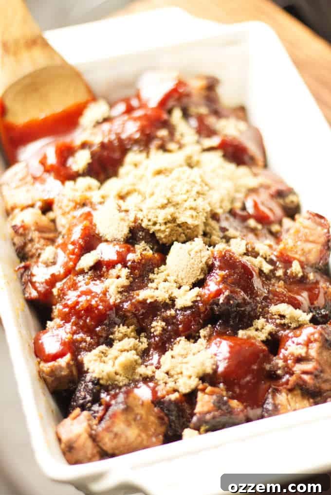 Tender brisket burnt ends, generously coated in a shimmering Kansas City-style BBQ sauce, resting in a white ceramic dish. A sprinkle of brown sugar adds a touch of sweetness and visual appeal.