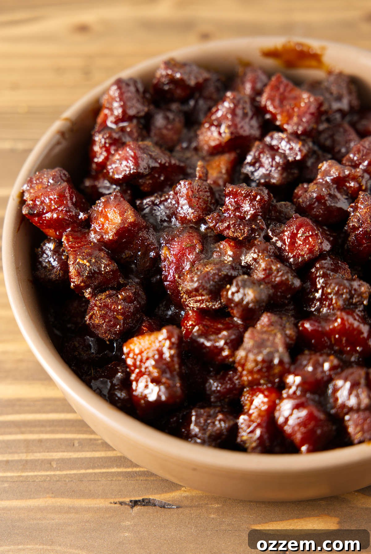 A large ceramic bowl filled to the brim with glistening, caramelized pork belly burnt ends, ready to be served.