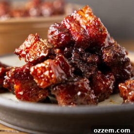 A close-up shot of perfectly stacked, glistening pork burnt ends on a plate, highlighting their rich color and tender texture.