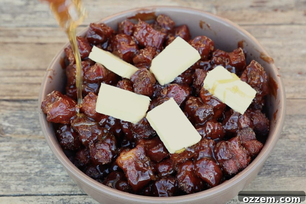 A baking dish filled with partially smoked pork belly cubes, with BBQ sauce, butter, and honey being added for the braising stage.