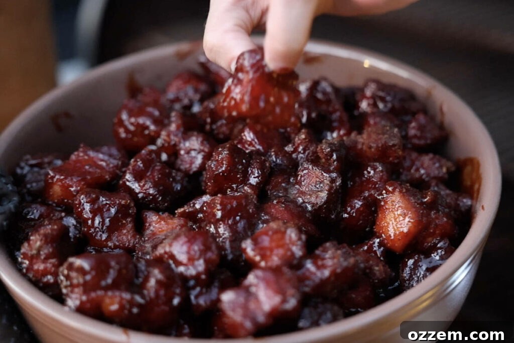 A close-up of a pan overflowing with perfectly finished pork belly burnt ends, glistening with caramelized sauce, after being removed from the smoker.