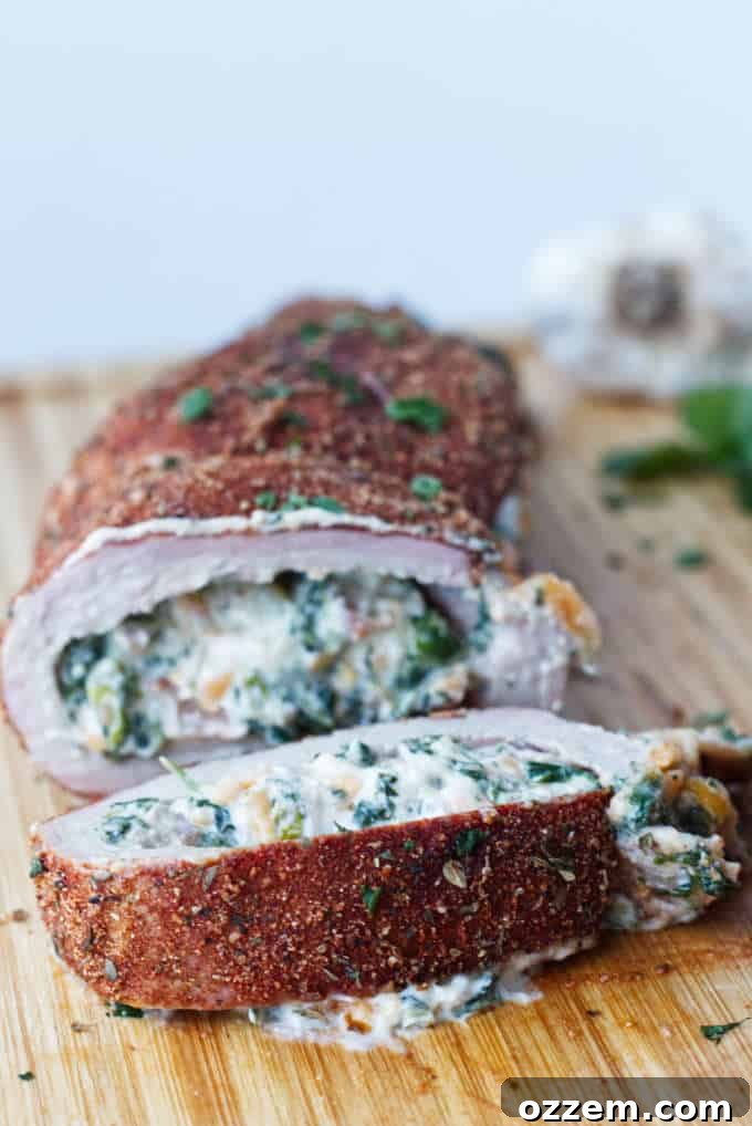 sliced stuffed pork tenderloin with cajun rub and twine holding it together, cheese stuffing, cilantro and garlic cloves sitting on wood