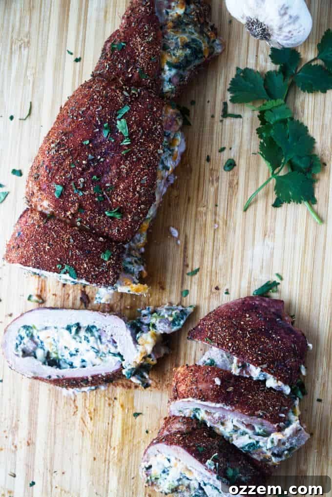 sliced stuffed pork tenderloin with cajun rub and twine holding it together, cheese stuffing, cilantro and garlic cloves sitting on wood