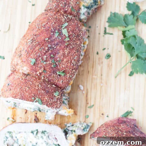 sliced stuffed pork tenderloin with cajun rub and twine holding it together, cheese stuffing, cilantro and garlic cloves sitting on wood