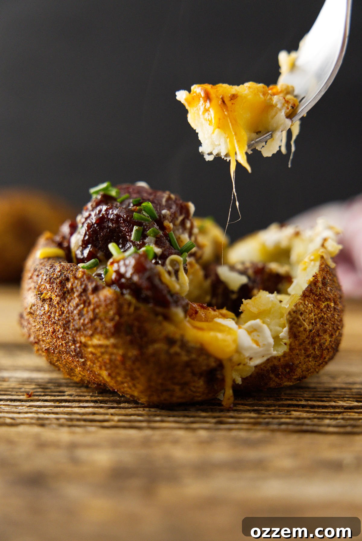 Fully loaded baked potato with a fork loaded with potato and melty cheese.
