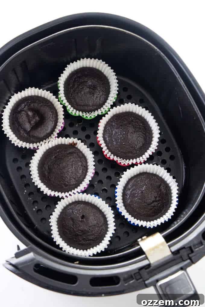 Six perfectly baked chocolate cupcakes nestled in an air fryer basket, ready to be frosted.