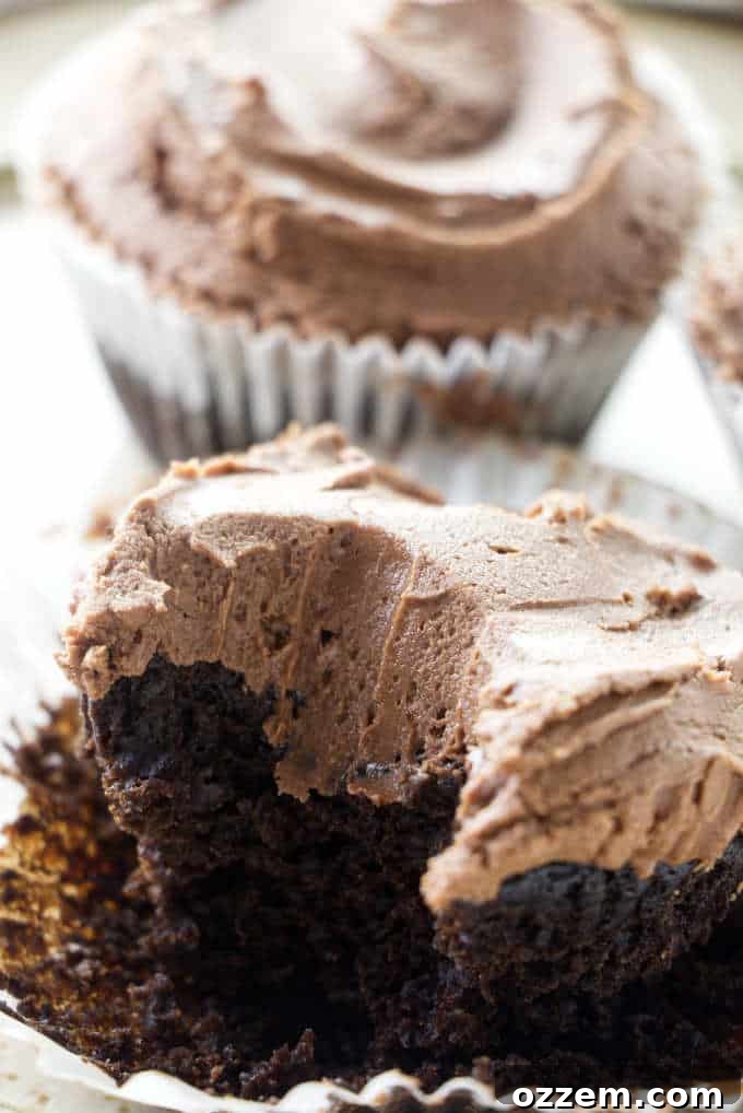 A chocolate cupcake with a generous swirl of chocolate buttercream, partially eaten to reveal its moist interior.