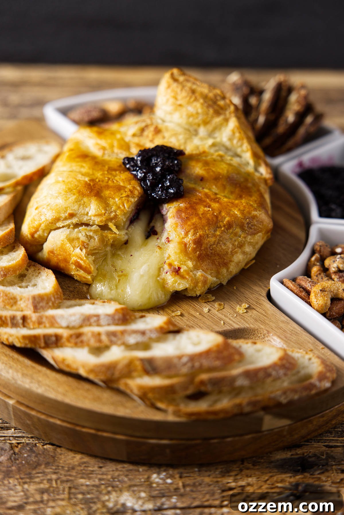 A glorious shot of crispy baked brie with irresistibly melty cheese spilling out, presented on a cutting board alongside a pot of jam and slices of fresh bread.