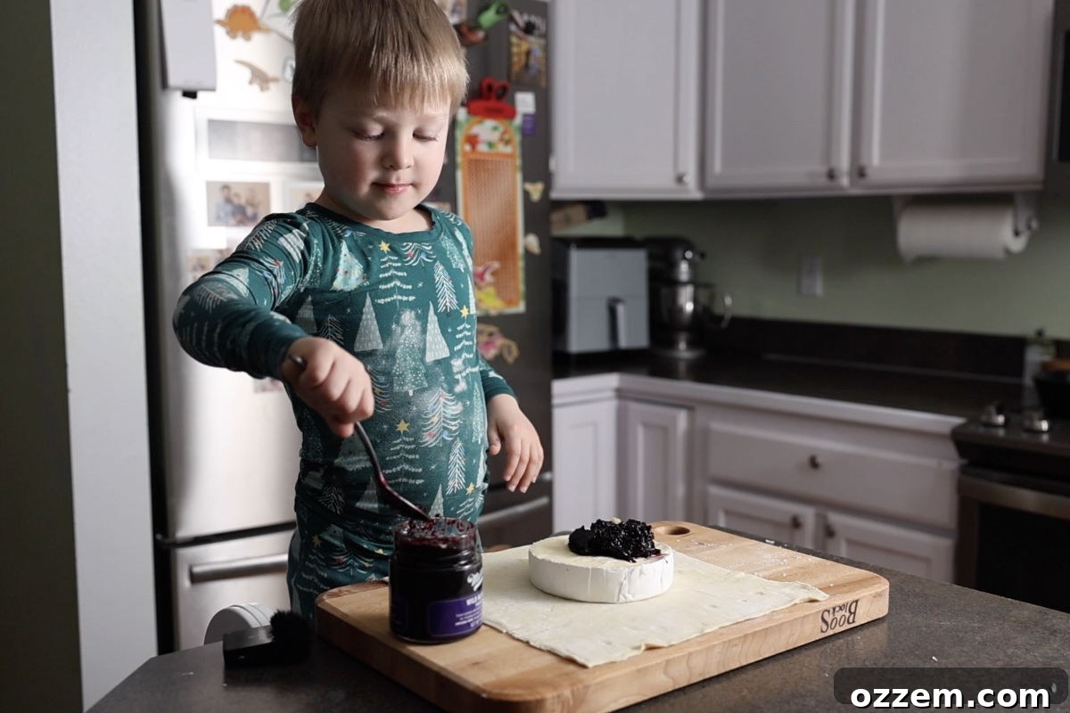 Applying a generous spoonful of wild blueberry preserves onto the top of the brie.