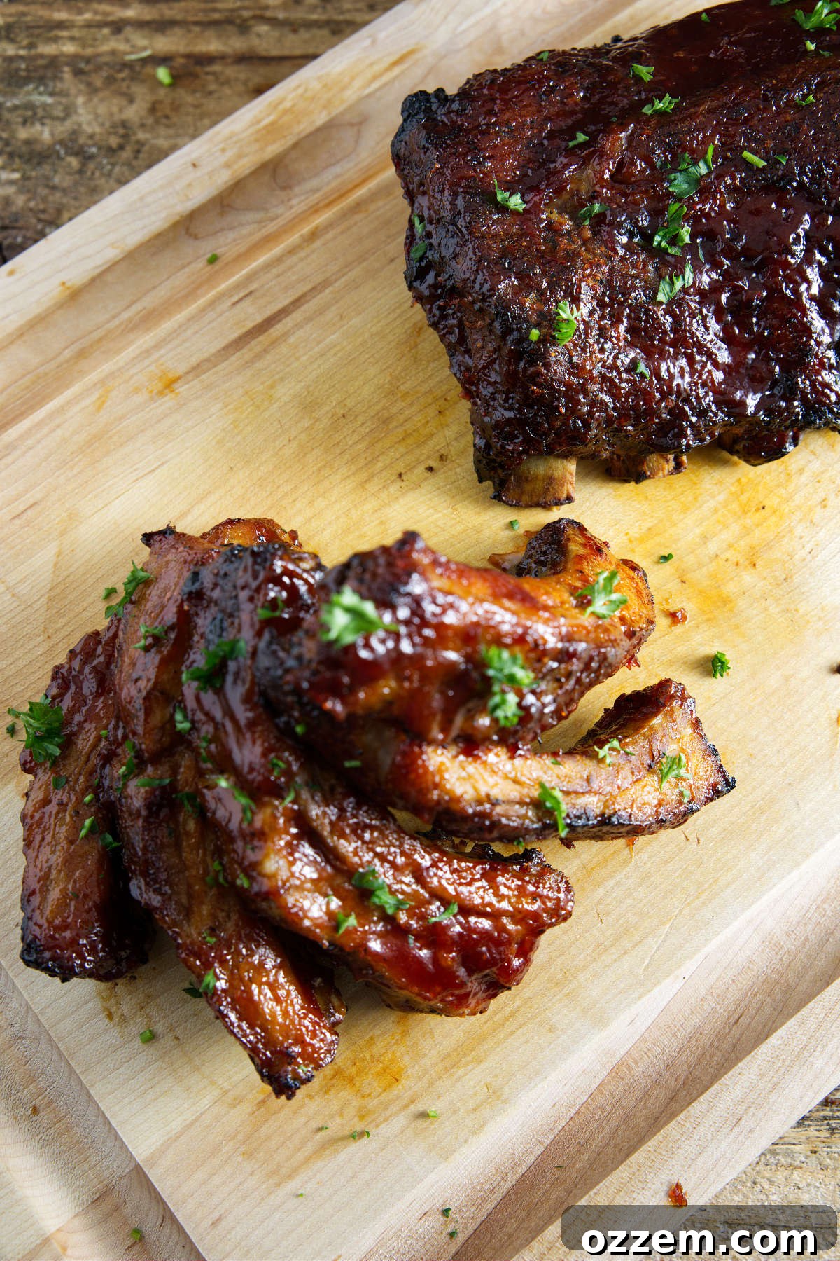 A whole slab of pork ribs and a stack of individually sliced ribs on a cutting board, ready for serving.