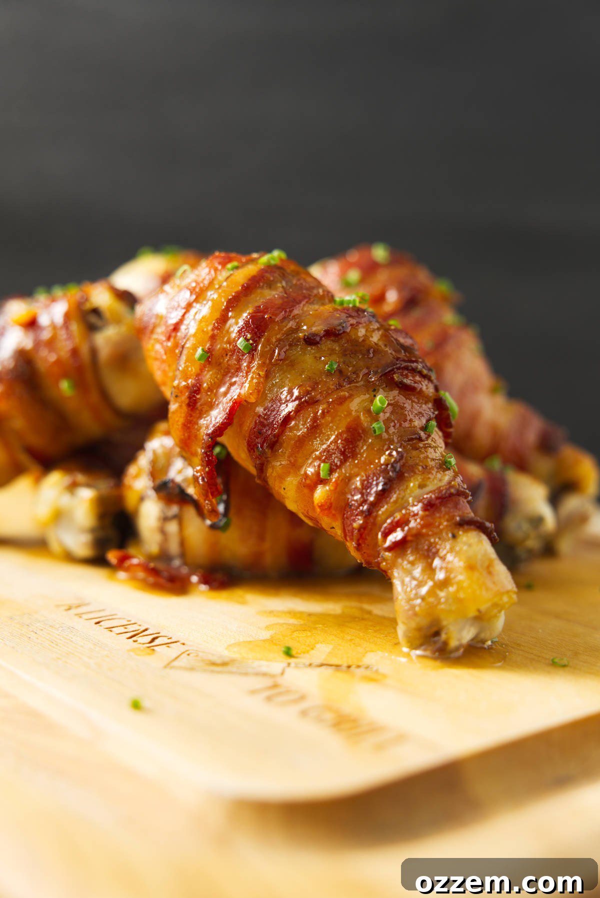 Smoky Traeger Stuffed Chicken Legs 4 Chicken legs wrapped in bacon stacked on a cutting board.