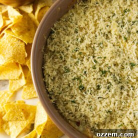 Smoked jalapeño popper dip with a bread crumb topping in a large bowl next to tortilla chips.
