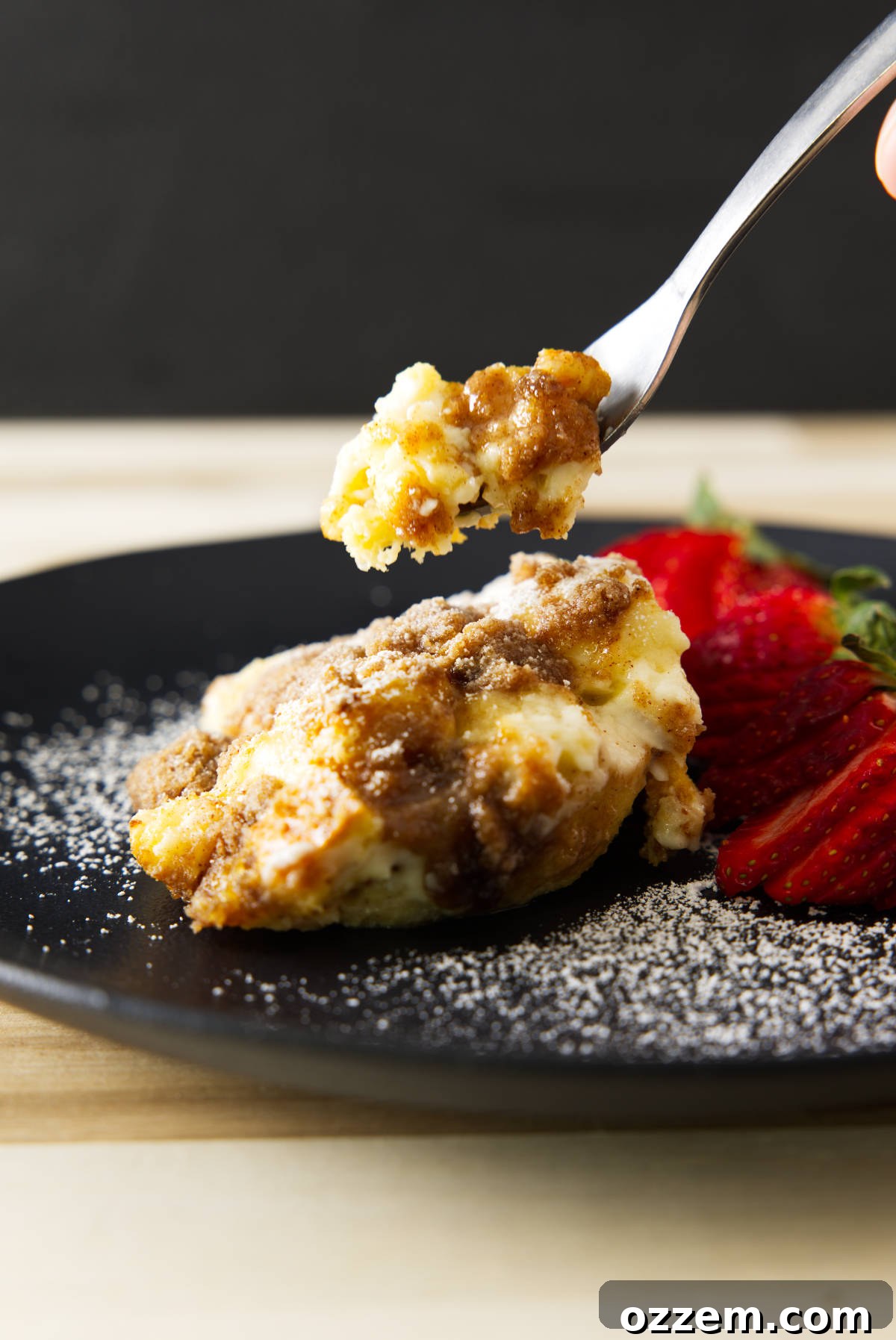 A fork taking a bite from a plated serving of overnight French toast casserole, showing the custardy interior and streusel topping.