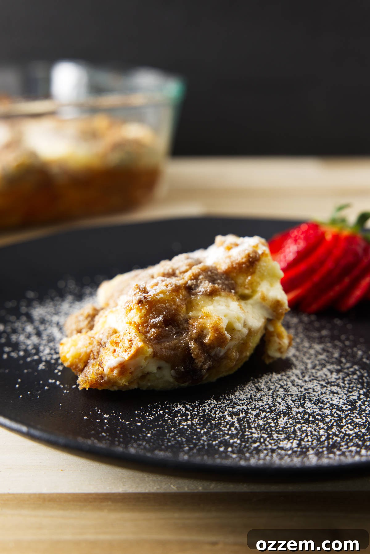 A scoop of golden-brown overnight French toast casserole on a white plate, dusted with powdered sugar, ready to be served.