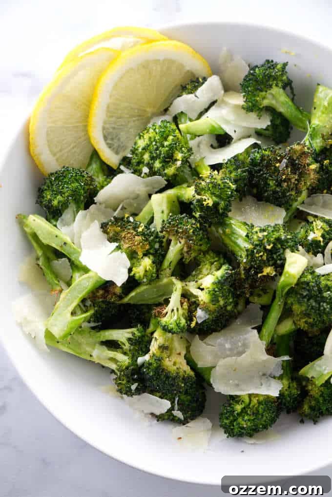 Crispy Lemon Parmesan Air Fryer Broccoli 5 A bowl of freshly cooked air fryer broccoli, garnished with grated parmesan cheese and lemon wedges.