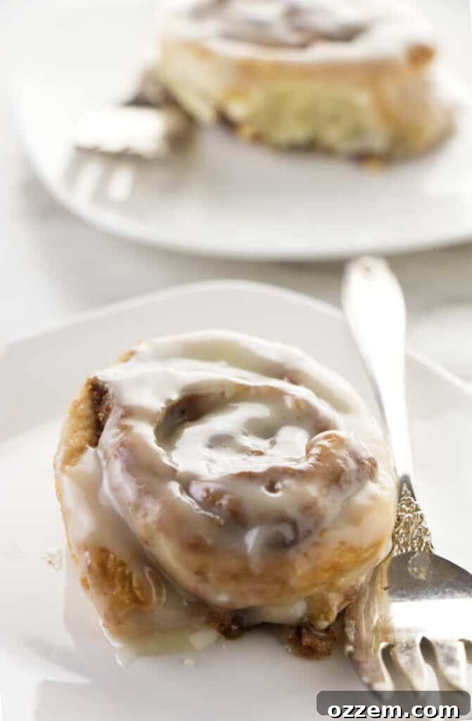 Close up of a no yeast air fryer cinnamon roll, golden brown and generously drizzled with cream cheese frosting, showing its soft interior.