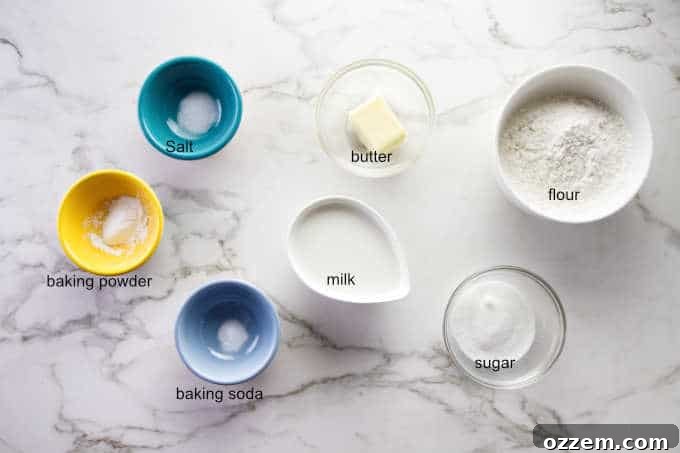 Ingredients laid out for no yeast cinnamon rolls, including flour, sugar, cold butter, whole milk, salt, baking soda, and baking powder, on a rustic wooden surface.