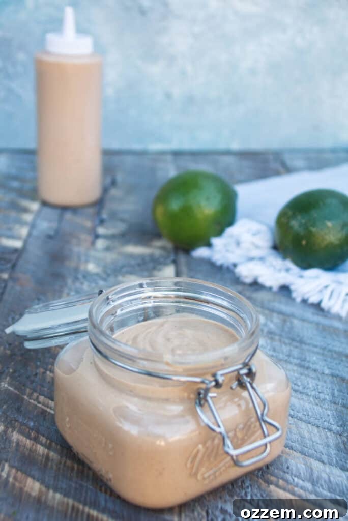 Homemade Chipotle Lime Crema in a mason jar, perfectly smooth and vibrant, resting on a rustic wooden surface with fresh limes in the background. The ideal sauce for adding a Mexican twist to grilled meats, tacos, and more.