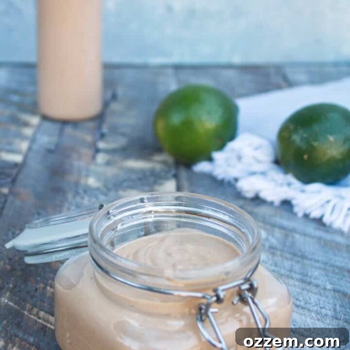 Vibrant Chipotle Lime Crema in a glass jar, ready to serve, with fresh limes in the background. A perfect condiment for grilling and Mexican cuisine.