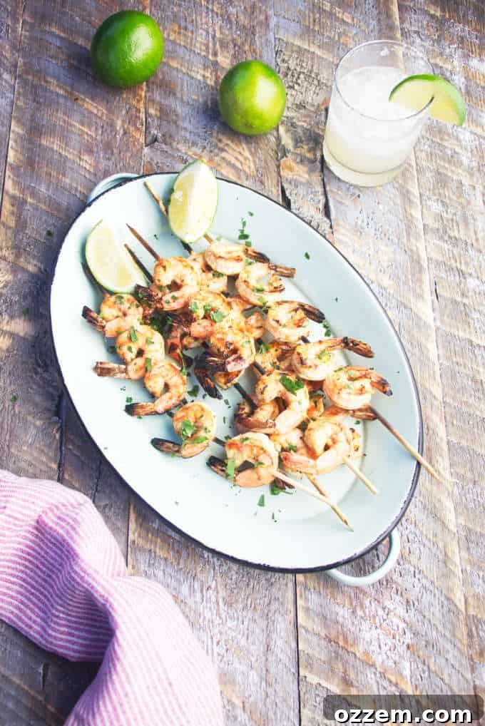 Platter of grilled tequila lime shrimp skewers, garnished with fresh limes, beside a glass of margarita