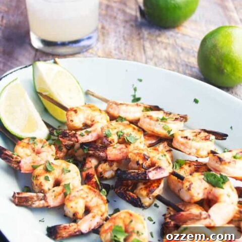 Grilled tequila lime shrimp on a skewer with lime wedges and margarita