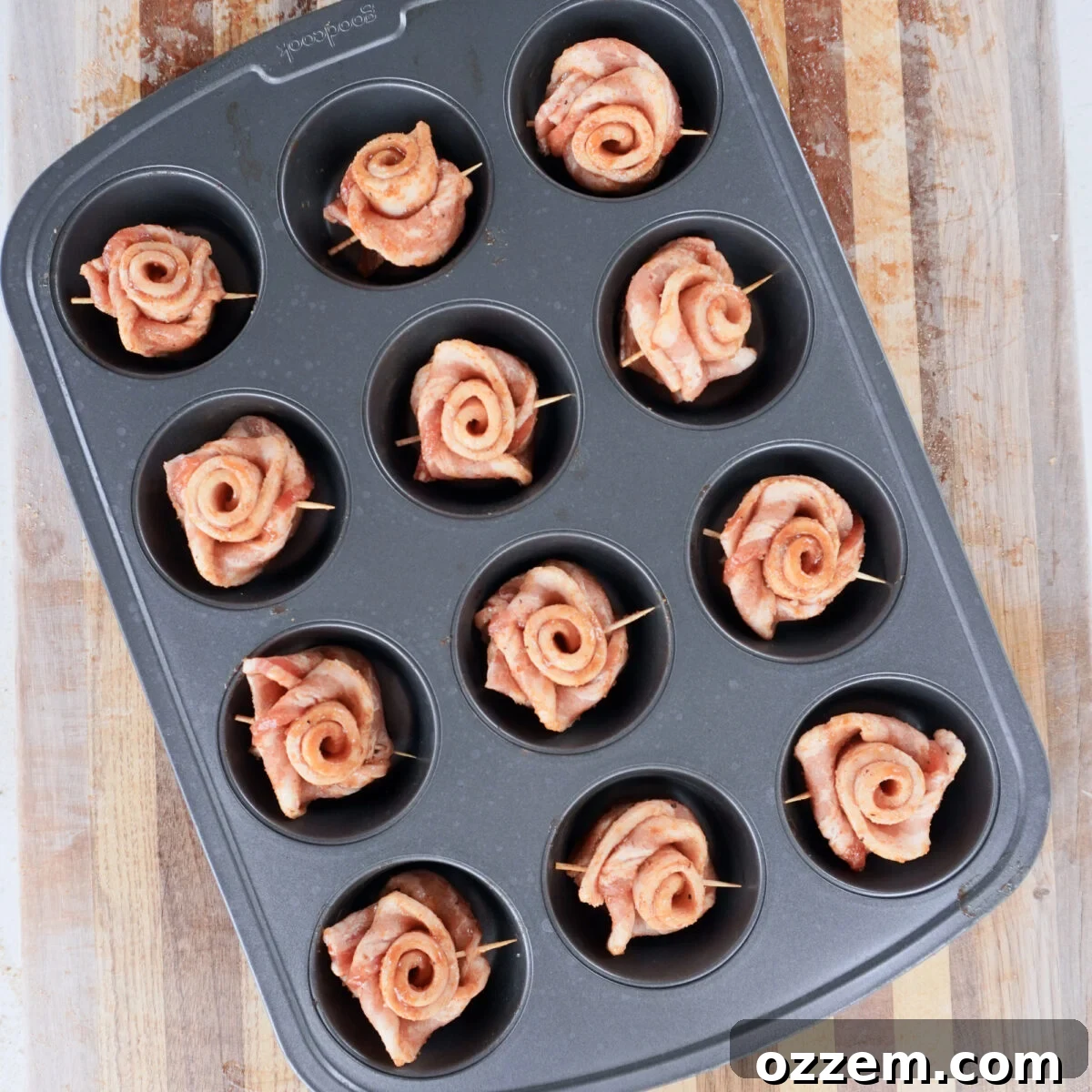Formed bacon roses arranged neatly in a muffin pan, ready for grilling.