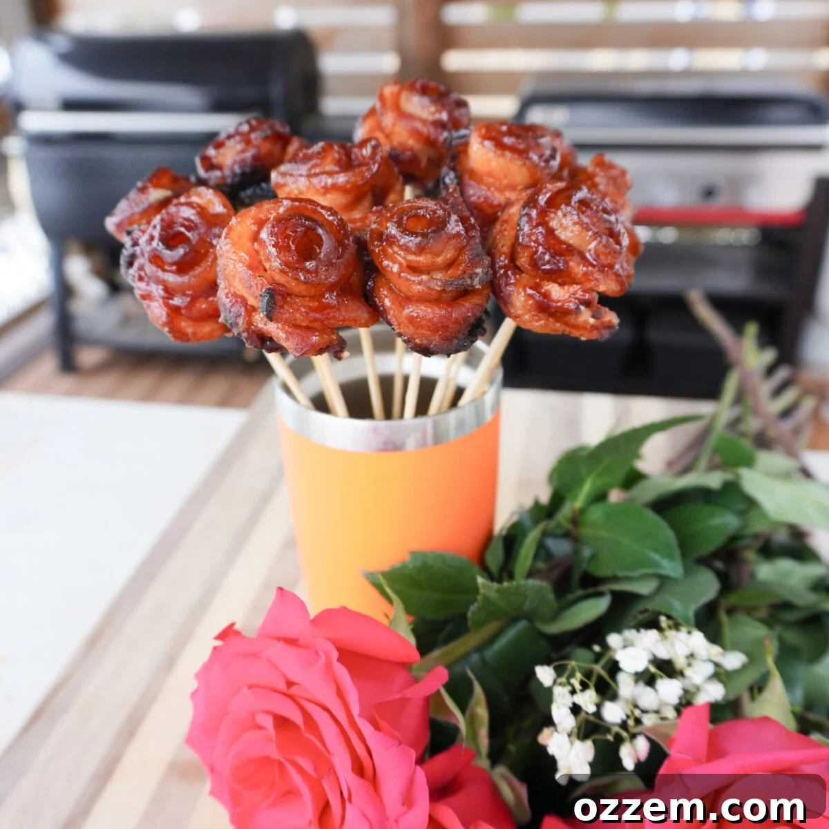 Grilled Bacon Roses artfully arranged in a Yeti Tumbler alongside fresh pink roses, a perfect blend of culinary and aesthetic appeal.