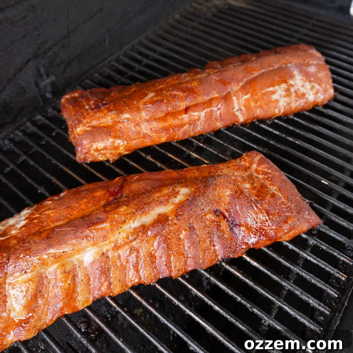 Baby back ribs smoking directly on the grates of a grill.
