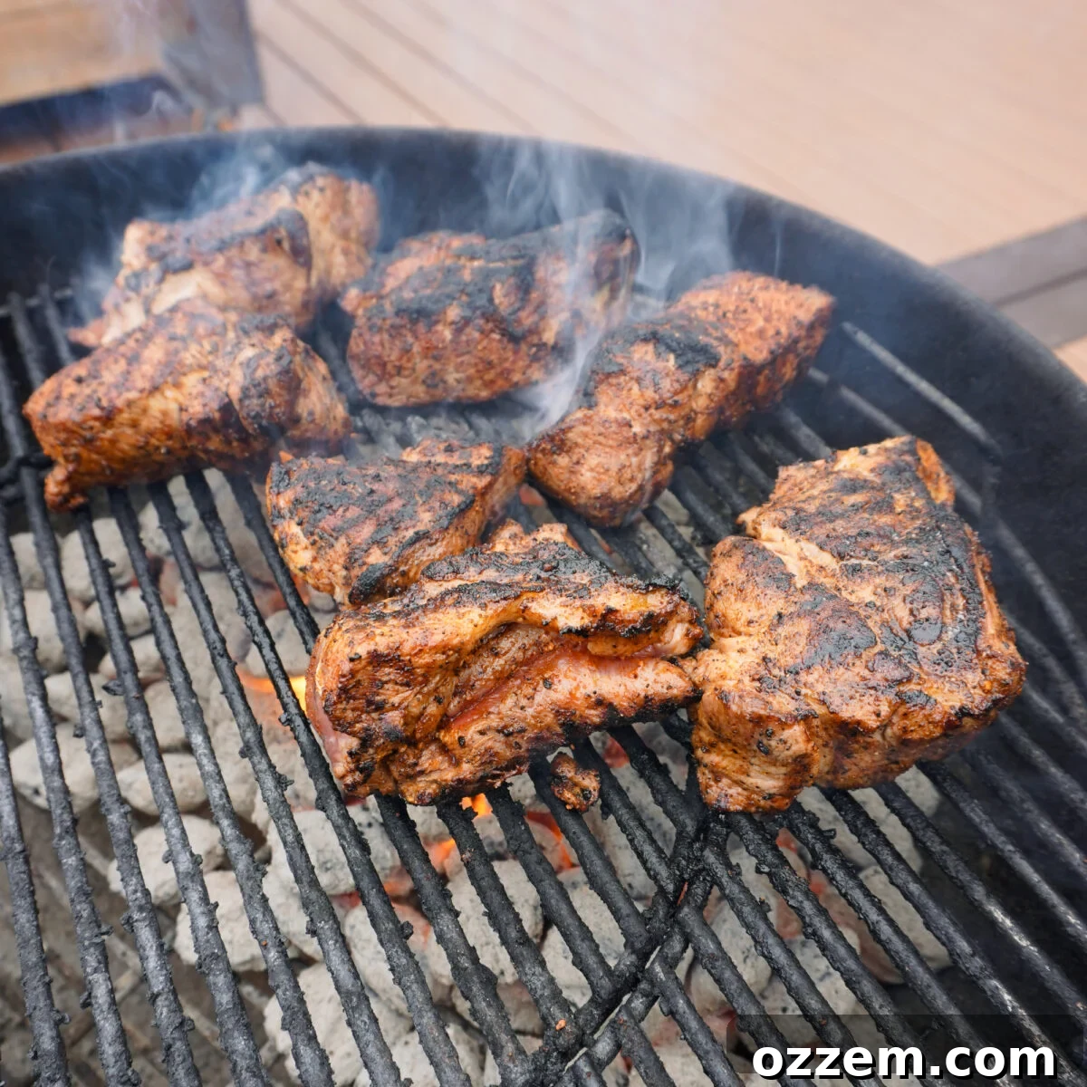Seared pork pieces cooking on a charcoal grill.
