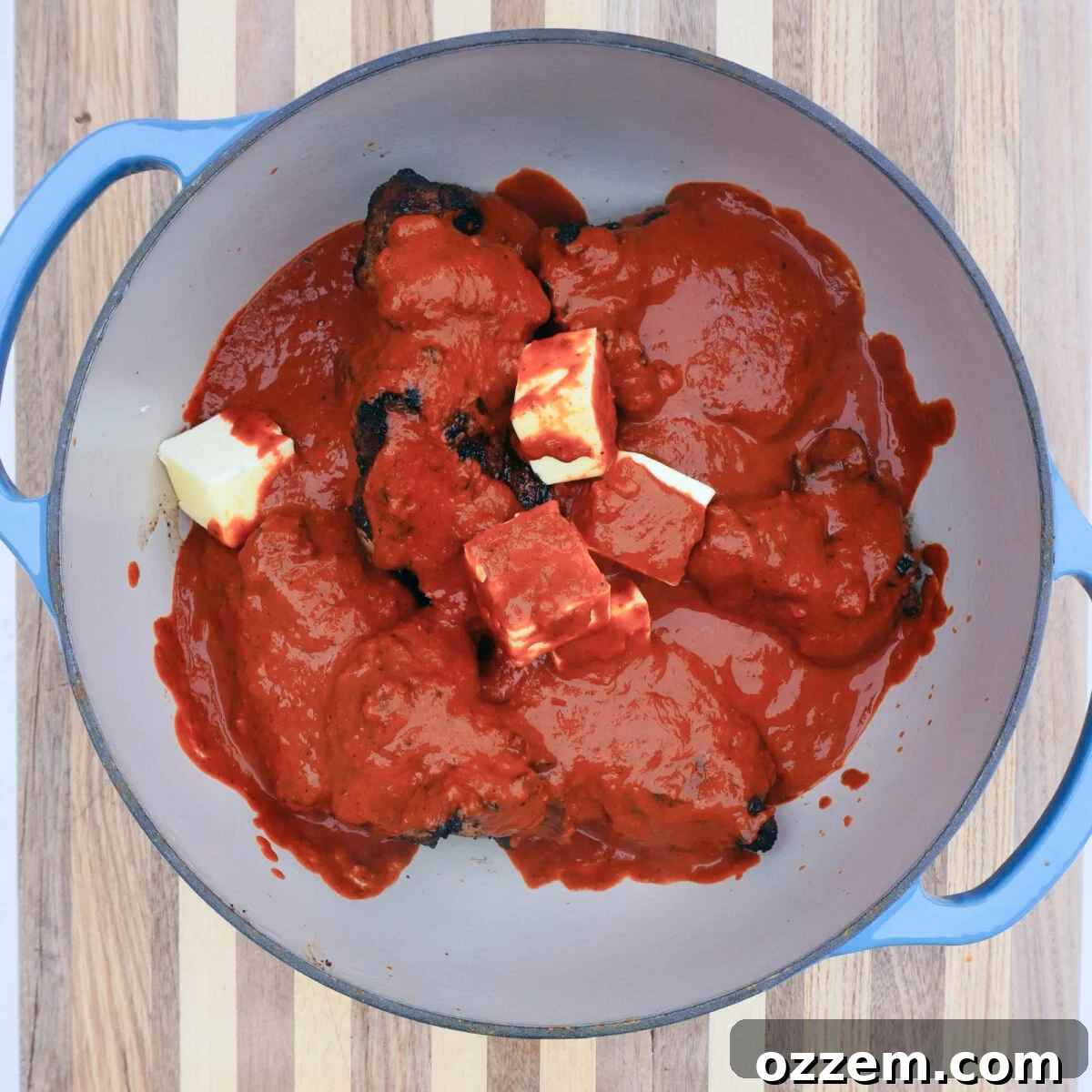 Seared pork shoulder chunks covered in adobo sauce in a Dutch oven on a grill.